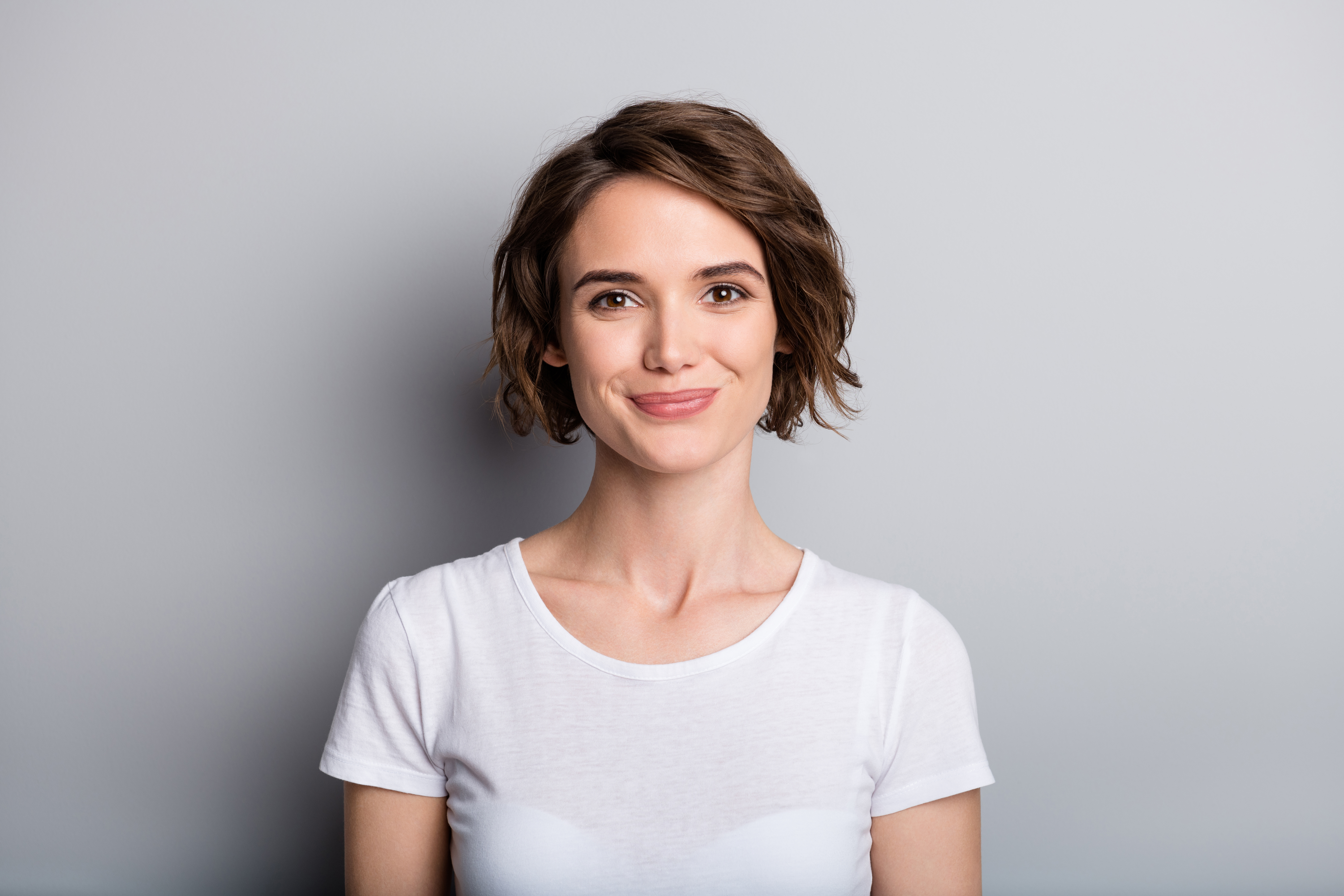 Portrait of young smiling charming cute girl woman female look in camera wear white t-shirt isolated on grey color background.